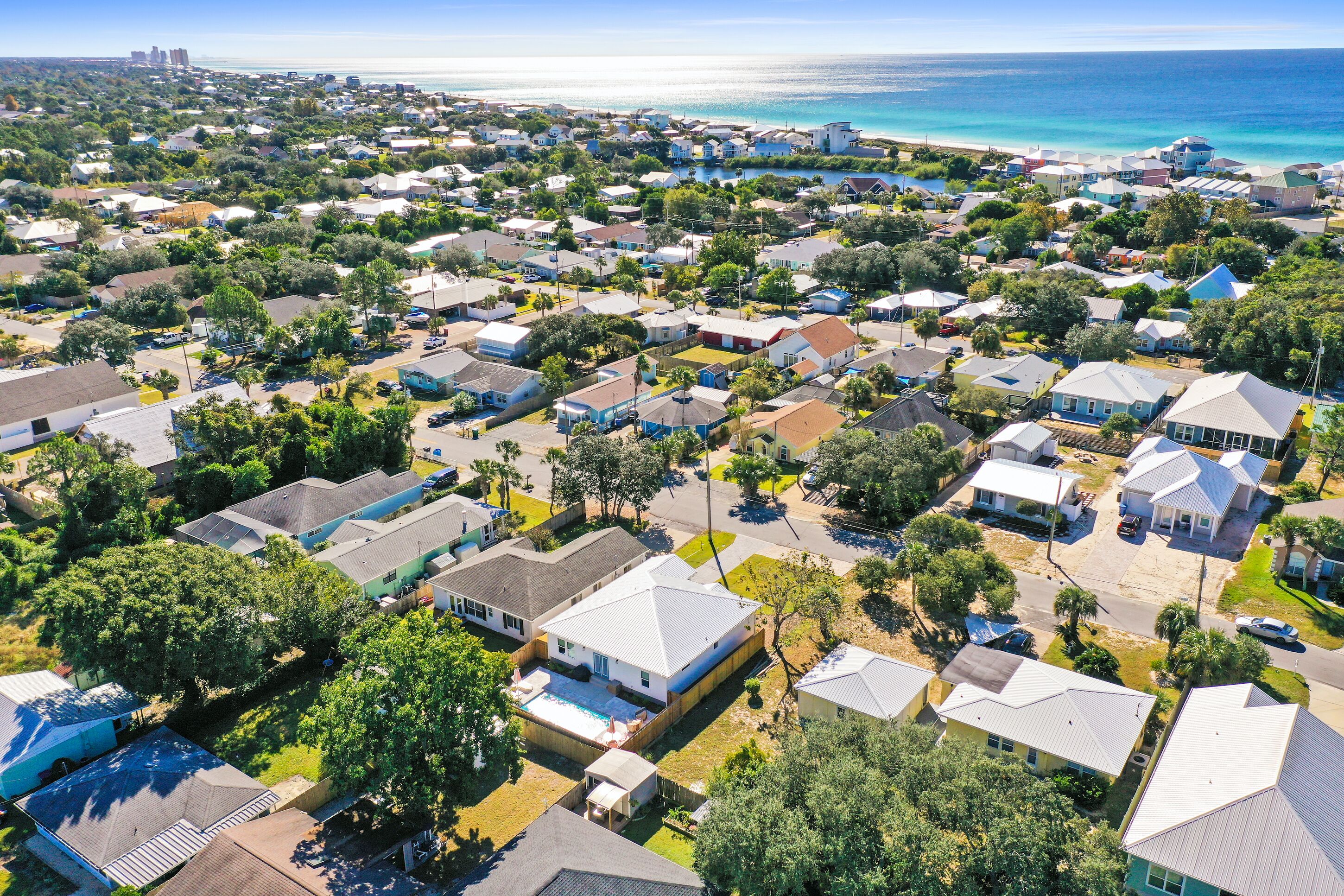 Vue aérienne d’un quartier résidentiel avec des maisons, des arbres et une plage en arrière-plan.