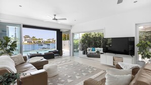 A modern living room with a large TV, comfortable seating, and a view of a pool and buildings.