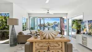 Relax in this stylish living area with a sofa, coffee table, and flat-screen TV, offering a view of the pool and surrounding buildings.
