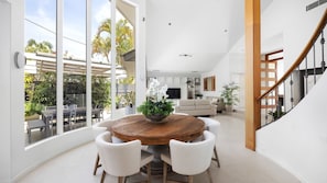 Relax in this open-plan living space with a central dining table, comfortable seating, and a view of the lush garden.