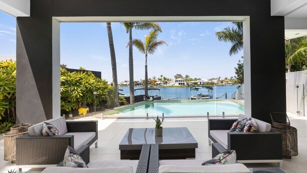 A modern outdoor seating area with a pool and a view of the water and palm trees.