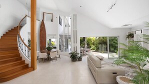 A spacious living area with a wooden staircase, a dining table with chairs, a sofa, and a large sliding glass door leading to a garden.