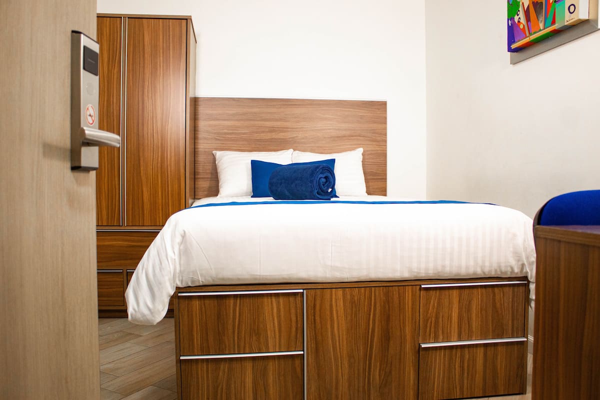 Una habitación de hotel con una cama de madera, cabecero blanco y una toalla azul.
