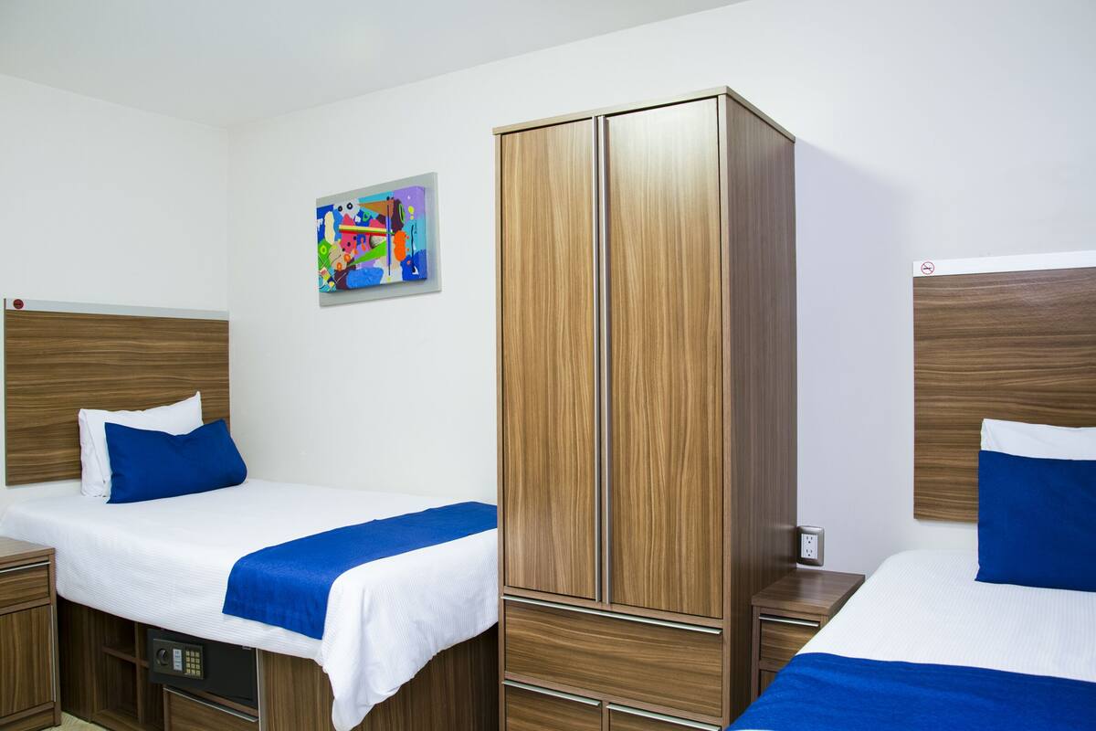Una habitación de hotel con dos camas, un armario y un cuadro de colores en la pared.