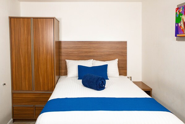 A hotel room with a wooden wardrobe, a bed with white and blue bedding, and a small bedside table. - La Casa Azul (Mexico City)