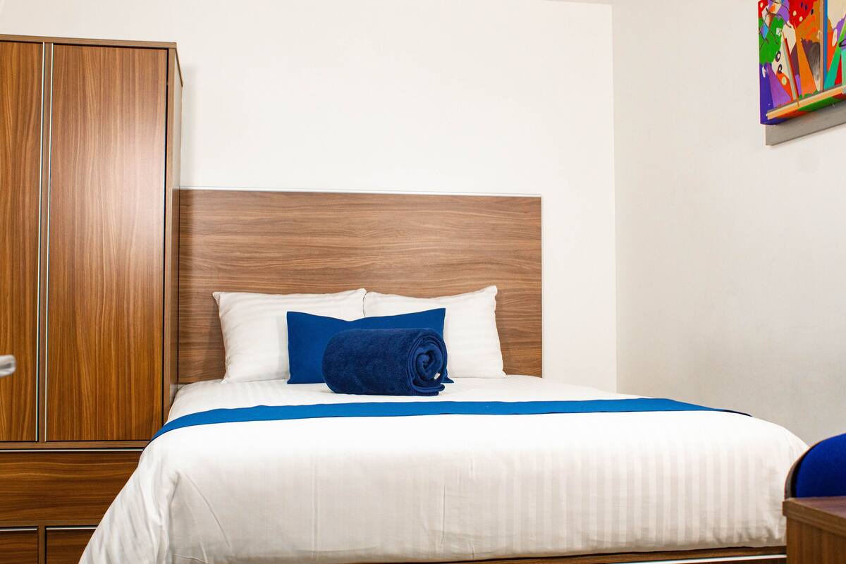 Una habitación de hotel con una cama, un armario de madera y un cuadro colorido en la pared.