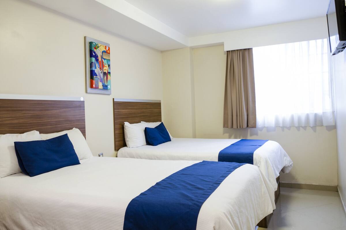 Una habitación de hotel con dos camas, cada una con una colcha azul y blanca, un cabecero de madera y un cuadro en la pared.
