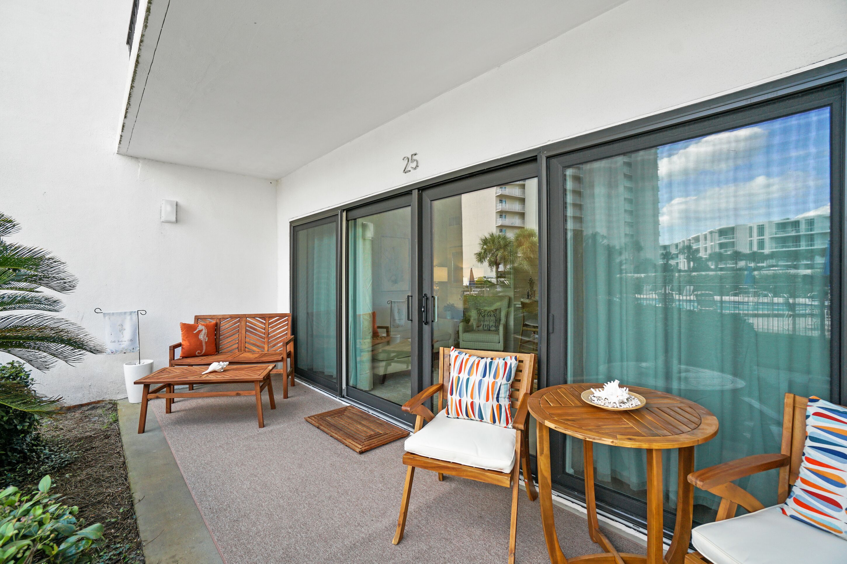 Un balcón con sofá, sillas, una mesa y vista a un edificio a trav és de puertas de vidrio.