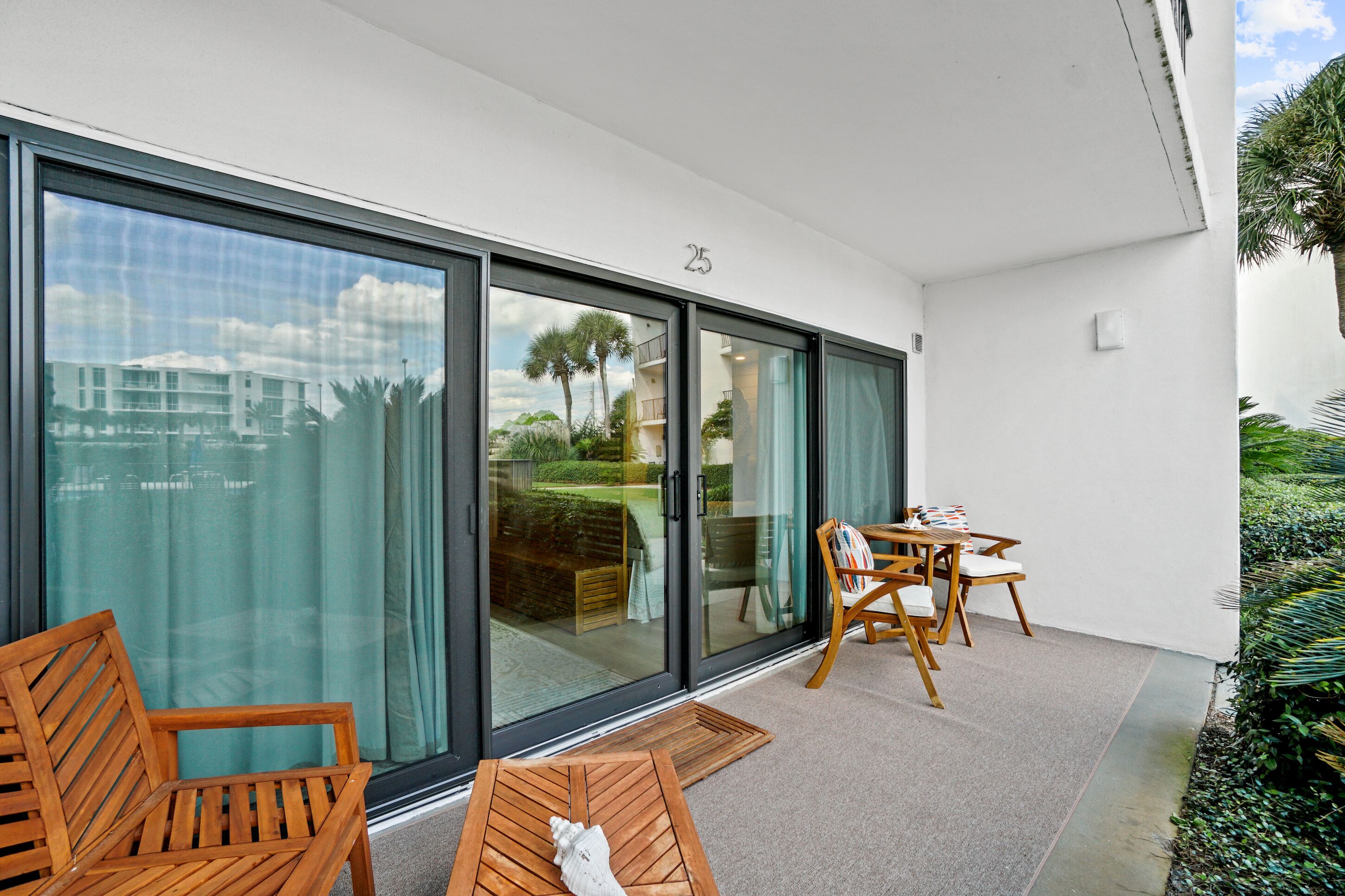 Ein moderner Balkon mit großer Glasschiebetür, Holzmöbeln und Blick auf eine Wohngegend.