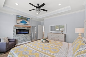 A bedroom with a bed, a TV, a fireplace, a ceiling fan, and a view of the outside. - Pearls by the Sea - Luxury Home in Atlantic Beach (North Myrtle Beach)