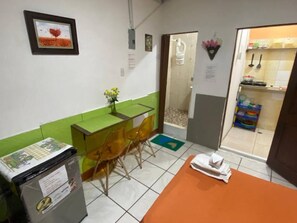 A small room with a green and white color scheme, a desk with a chair, a small table with a towel, and a shower area visible through a glass door. - Mini Suite en Garzota Norte / independiente  (Guayaquil)