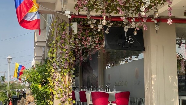 Een buitenterras met rode stoelen en een tafel, omgeven door groen en bloemen.