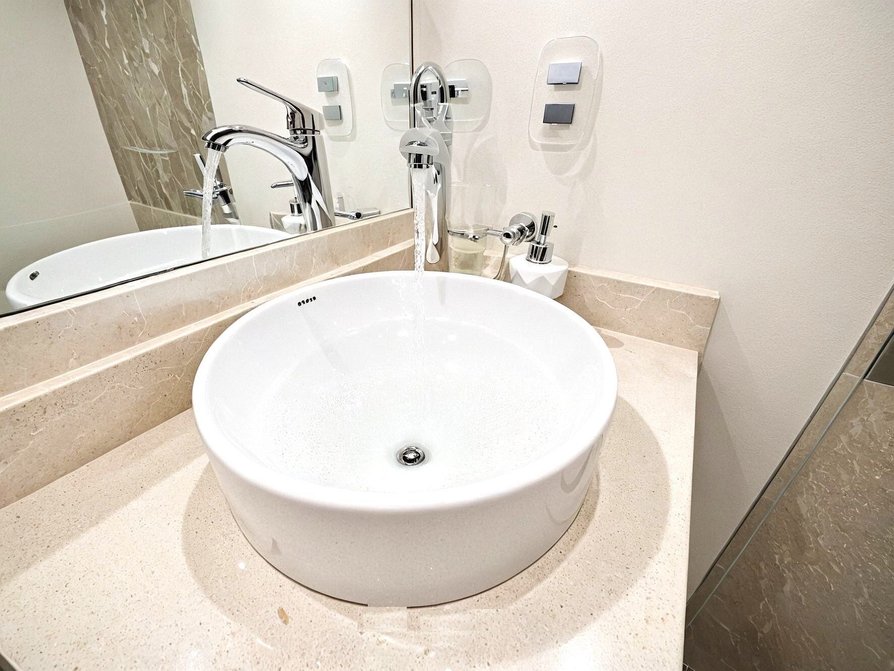 A modern bathroom with a round white sink, chrome faucets, and a large mirror.