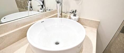 A modern bathroom with a round white sink, chrome faucets, and a large mirror.