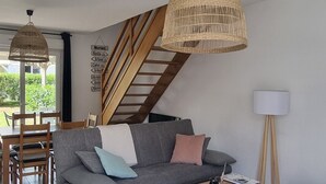 Ein modernes Wohnzimmer mit grauem Sofa, Holz-Couchtisch, Korbtreppe und einer Hängeleuchte.