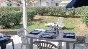 Eine überdachte Terrasse mit Tisch für zwei Personen, weißen Plastikstühlen und einem blauen Sonnenschirm.