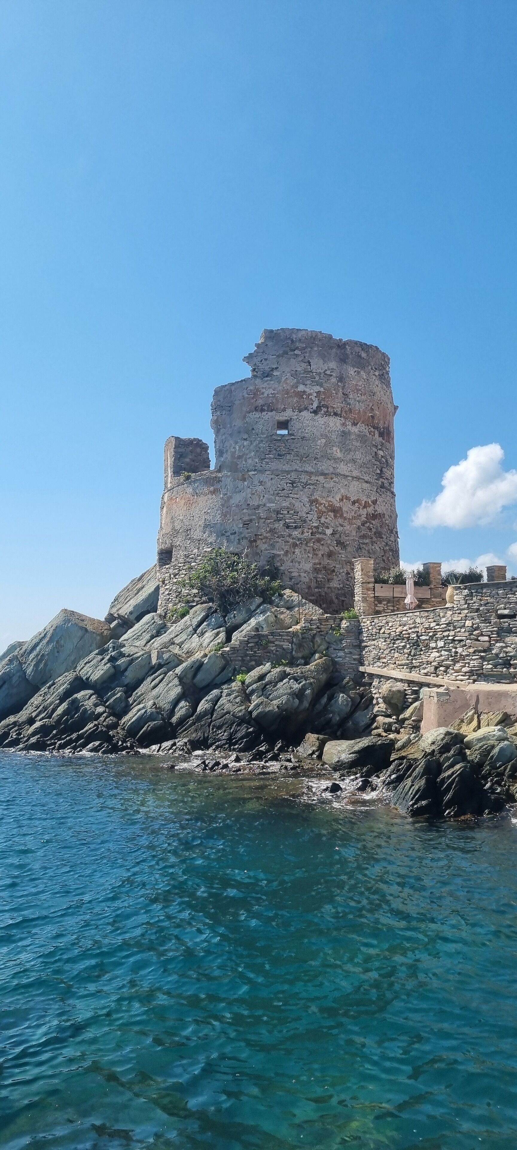 Eine historische Steinburg an einer felsigen Küstenlinie mit klarem, blauem Wasser.