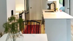 A modern kitchen with a central island, a dining area with a red patterned rug, and a hanging light fixture. - Quiet, convenient & Modern Haven (Gainesville)