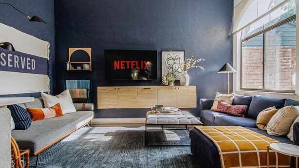 A modern living room with a dark blue accent wall, a Netflix sign, a wooden cabinet, a sofa, and a coffee table. - Quiet, convenient & Modern Haven (Gainesville)
