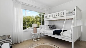 A bunk bed room with a window, a small table with a lamp, and a rug.