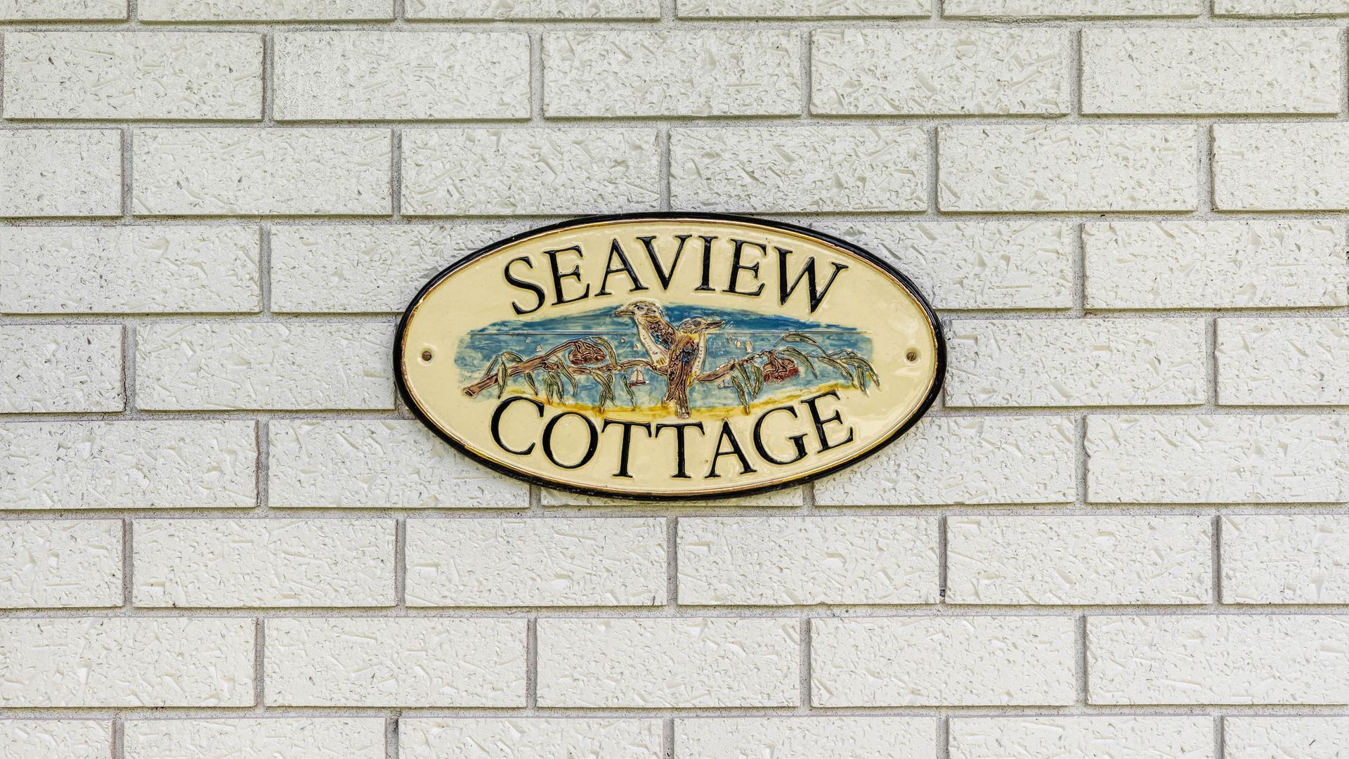 Une pancarte avec l’inscription « Seaview Cottage » sur un mur en briques blanches.