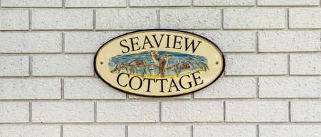 Une pancarte avec l’inscription « Seaview Cottage » sur un mur en briques blanches.