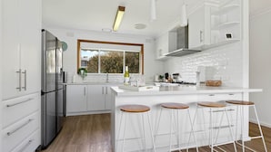 A modern kitchen with white cabinetry, a stainless steel refrigerator, a large window, and a bar area with stools.