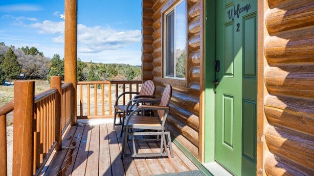 A log cabin with a green door labeled "Welcome 2", a wooden deck with chairs, and a view of the surrounding landscape. - Peaceful Cabin with Spectacular Stargazing Hot Tub (Alton)