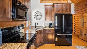 A kitchen with wooden cabinets, a black refrigerator, a microwave, and a stove. - Peaceful Cabin with Spectacular Stargazing Hot Tub (Alton)
