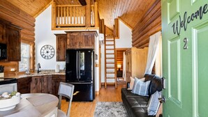 A log cabin interior with a kitchen, dining area, and a living room with a green door marked "Welcome". - Peaceful Cabin with Spectacular Stargazing Hot Tub (Alton)