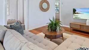 Un saló modern amb un sofà beix, una taula de centre de fusta rodona, una planta en test i un televisor de pantalla plana sobre un suport de fusta.