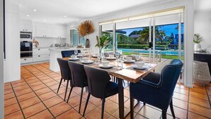 A modern kitchen with white cabinets, a dining table set for four, and a large sliding glass door leading to a pool. - Waterfront Capri -Walk to cafes by Bnbbooking (Surfers Paradise)
