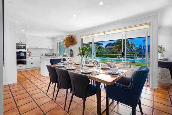 A modern kitchen with white cabinets, a dining table set for four, and a large sliding glass door leading to a pool.