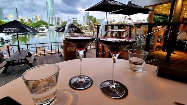 A table with two martini glasses and a water glass, overlooking a marina with boats and a city skyline. - Waterfront Capri -Walk to cafes by Bnbbooking (Surfers Paradise)