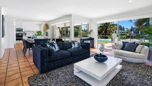 A spacious living area with a dark blue sofa and a white coffee table, a light-colored sofa, and a large window offering a view of the outdoors. - Waterfront Capri -Walk to cafes by Bnbbooking (Surfers Paradise)