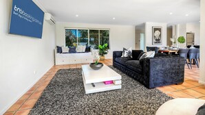 A modern living room with a white sofa, a black sofa, a white coffee table, and a dining area with chairs and a table. - Waterfront Capri -Walk to cafes by Bnbbooking (Surfers Paradise)