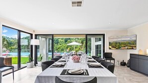 A dining area with a table set for six, large windows, and a view of a natural landscape.