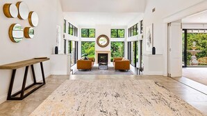 A spacious foyer with a fireplace, two sofas, a wooden bench, and a large chandelier.