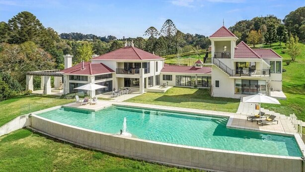 A large, modern house with a swimming pool, multiple balconies, and a well-maintained lawn.
