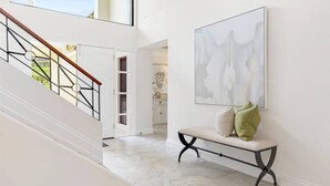 A spacious hallway with a marble floor, a staircase with a wooden handrail, and a bench with cushions.