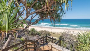 Una terraza de madera que conduce a una playa con vistas al océano, rodeada de vegetación tropical.