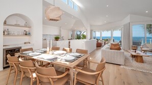 Amplia sala de estar con una mesa de comedor para cuatro, una cocina con armarios blancos y un balcón con vistas al océano.