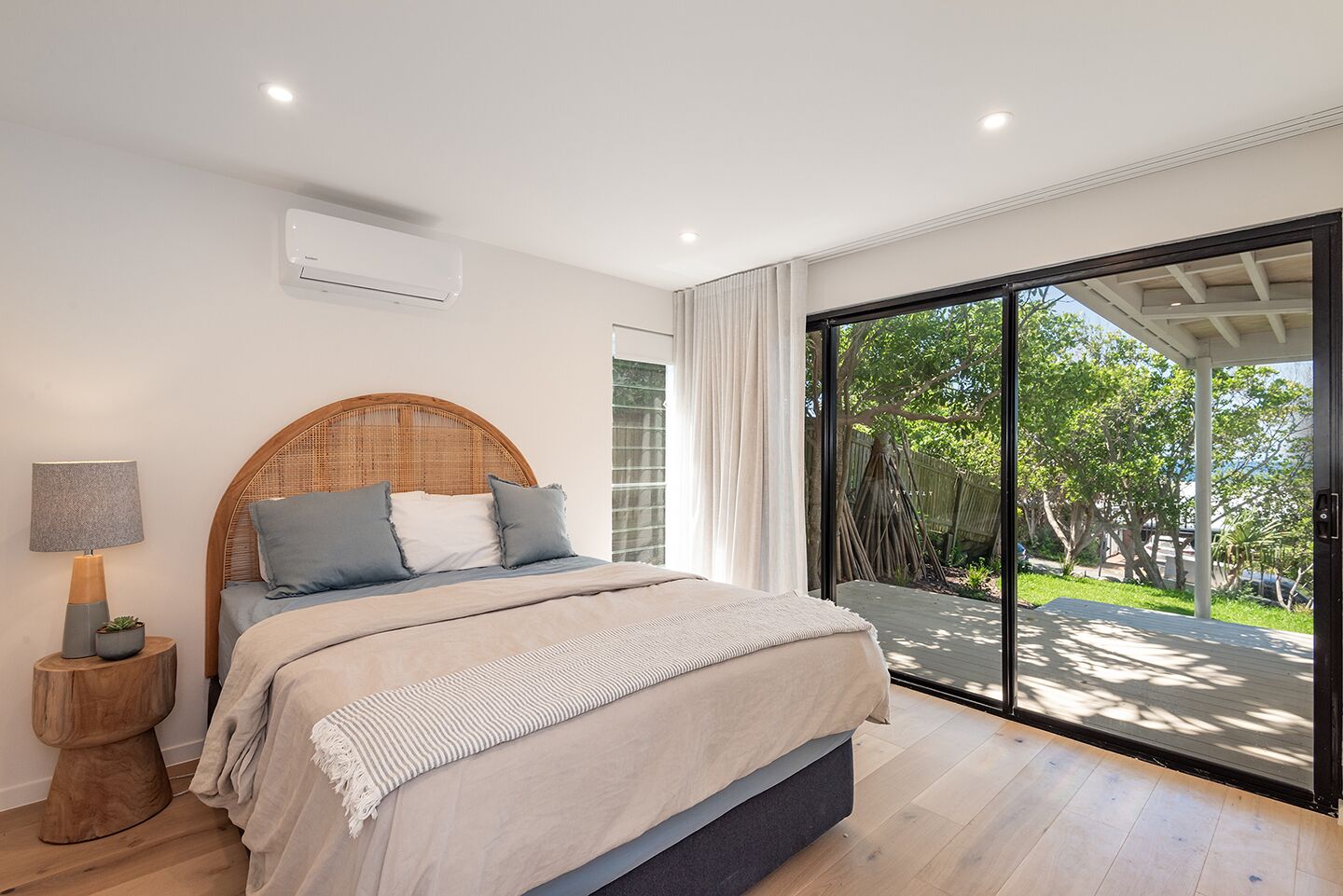 A bedroom with a large bed, a bedside table with a lamp, and a view of the outdoors through a sliding glass door.