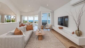 Un salón amplio con un sofá grande, una mesa de centro y un televisor instalado en la pared.