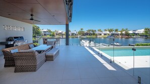 A modern outdoor patio with a grill, wicker furniture, and a view of a marina and lake.