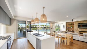 A modern kitchen with a central island, a dining area with wooden chairs, and a living area with a sofa and TV.