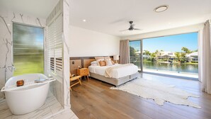 A modern bedroom with a large bed, a bathtub, and a view of a body of water.