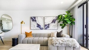 Un salon moderne avec un canapé d’angle gris, une table basse en marbre blanc et une grande plante verte.