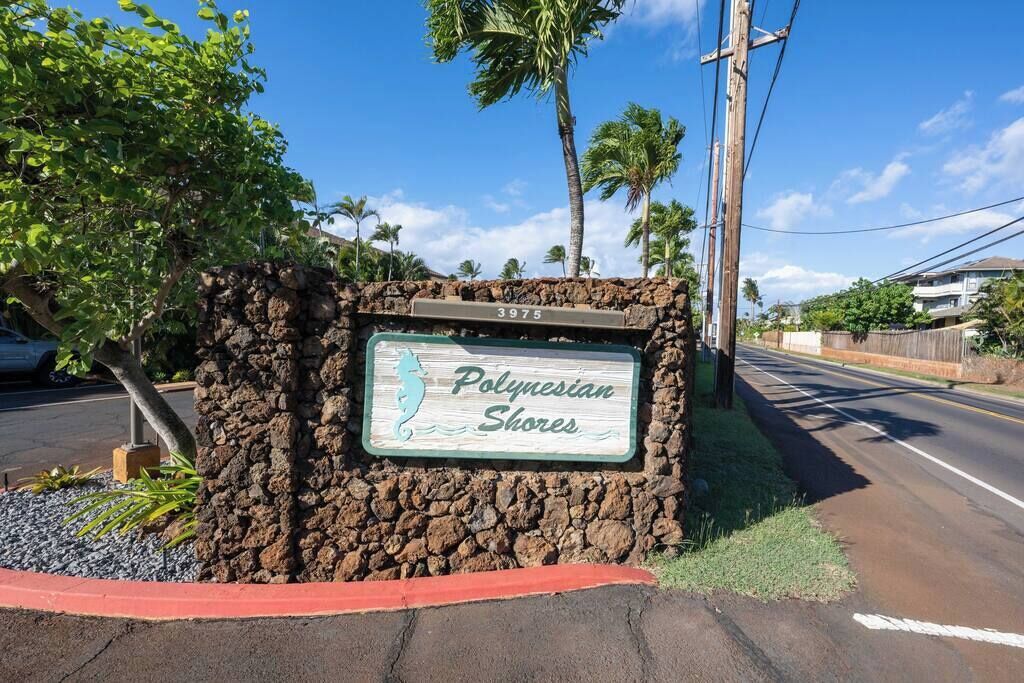 Ein Schild für 'Polynesian Shores' mit der Nummer '3975', vor blauem Himmel, Palmen und einer Straße.