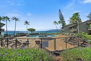 A pool area with lounge chairs, a circular pool, and a view of the ocean. - Coral Cove-Poolside Condo and Panoramic Ocean View (Lahaina)